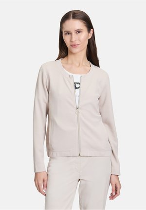 Lys beige zip-jakke lavet af et tekstureret, åndbart stof. Har en rund halsudskæring, lange ærmer og sidelommer.