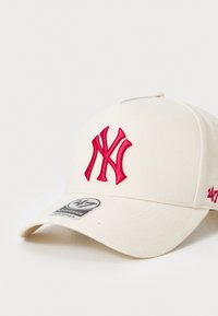 Cream baseball cap featuring a raised red embroidered New York Yankees logo, with a curved brim and an adjustable strap at the back.