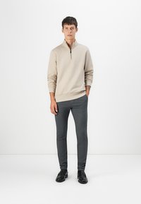 Beige zip-neck sweater with long sleeves, paired with dark gray slim-fit trousers. Black shoes complete the outfit. Simple and modern design.