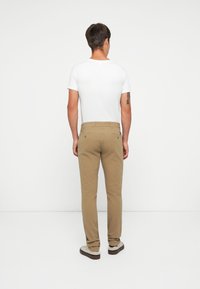 Slim fit khaki nadrág sima textúrával és klasszikus zsebekkel, fehér, egyszínű pólóval és laza bézs cipőkkel párosítva.
