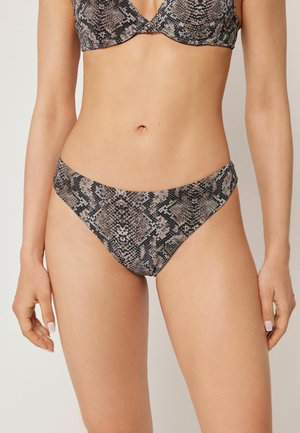 Kobieta nosząca bikini z wysokim stanem i dopasowanym stanikiem z fiszbinami z brązowym i czarnym wzorem węża.