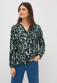Blouse à manches longues avec un imprimé animal abstrait noir, vert et beige. Le décolleté en V et les manches froncées enrichissent le design.