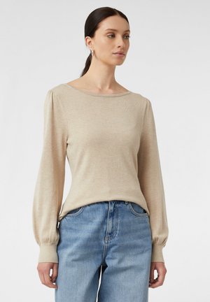 Maglione lungo beige chiaro a maniche lunghe con scollatura a barca, caratterizzato da dettagli arricciati sulle spalle e polsini a coste, abbinato a jeans blu.