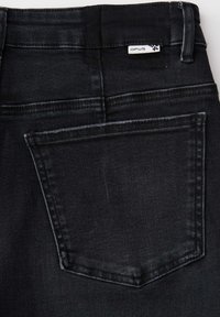 Back view of black denim jeans showing a single stitched back pocket and a small white brand label reading OPUS size 24.