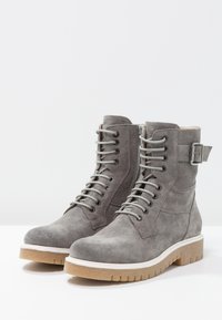 Harmaat mokkasiinit nilkkakengät pyöreillä kärjillä, nauhoilla ja solk yksityiskohdalla. Paksu, teksturoitu kumipohja, jossa on kontrastoiva vaaleanruskea väri.