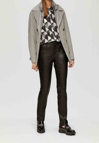 Szary podwójnie zapinany płaszcz z szerokim kołnierzem, noszony na czarno-białą wzorzystą koszulę, w połączeniu z błyszczącymi czarnymi skórzanymi spodniami i mokasynami.