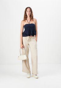Haut sans bretelles bleu marine avec un ourlet volanté, associé à un pantalon large beige. Petit sac à main blanc. Modèle portant des baskets claires.