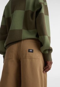 Maglione a scacchi verde e marrone con una vestibilità rilassata, abbinato a pantaloni a gamba larga beige con marchio sulla tasca posteriore destra.