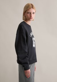 Czarna bluza z okrągłym dekoltem, w oversize'owym kroju, z białym nadrukiem. Zestawiona z szarymi spodniami z wysokim stanem, o gładkiej fakturze.