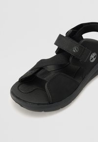 Sorte sandaler med justerbar rem, polstret sål, struktureret fodbund og gummiyderside. Har brandlogo på siden.