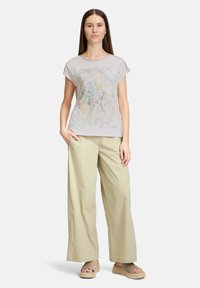 Lichtgrijze t-shirt met korte mouwen en kleurrijk grafisch ontwerp. Gecombineerd met losse beige broeken en tan platform sandalen.