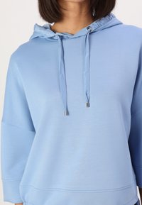 Sudadera azul clara con capucha, cordones con puntas metálicas, mangas tres cuartos y una textura suave y lisa.