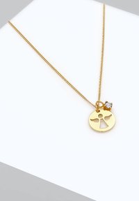 La collana d'oro presenta un pendente circolare con un design a intaglio e ali d'angelo, accentuato da un piccolo smeraldo trasparente. La catena è sottile e delicata.