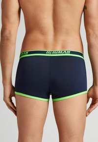 Marinblå boxershorts med grön midja och kant. Tillverkade av mjukt material, med en logotyp på midjan. Enkel, åtsittande design.