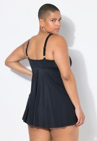 Svart baddräkt med justerbara axelband, A-linjeformad design, slät textur och utsvängd kjol. Har smala band och en figurnära bodice.