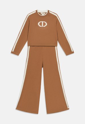 Brązowy zestaw odzieży do relaksu, składający się z krótkiego topu z długim rękawem i spodni o szerokich nogawkach, z białymi paskami i haftowanym logo.