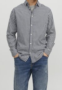 Camicia a quadri blu navy e bianca con bottoni, colletto, maniche lunghe e vestibilità comoda, abbinata a jeans blu con dettaglio usurato.