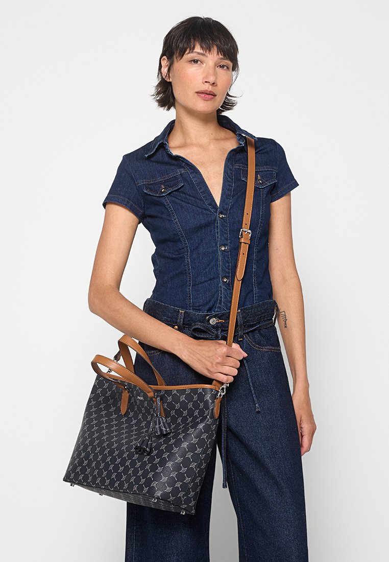 Graue Ledertasche mit geometrischem Muster, braunen Ledergriffen und verstellbarem Schulterriemen. Mit einem dekorativen Quasten-Detail.