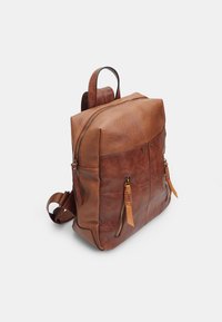 Zaino in pelle marrone con forma strutturata, dotato di due scomparti con zip, tasche laterali e dettagli in pelle naturale.