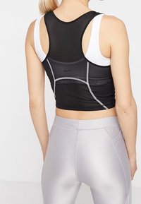 Haut de sport en maille noire avec une coupe ajustée, présentant des accents blancs et un dos nageur, associé à des leggings argentés brillants.