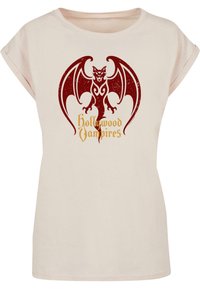 Lys beige t-skjorte med rullet erme som har et rødt flaggermusmotiv og teksten "Hollywood Vampires" i gull. Glatt stoffstruktur.