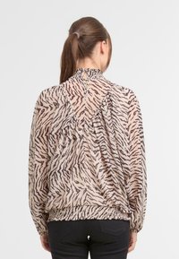 Bluzka z długim rękawem w beżowym kolorze z czarnymi prążkami w tygrysie, z elastycznym pasem, dekoltem w kształcie łezki z tyłu oraz marszczeniami.