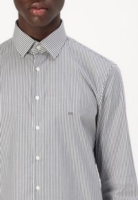 Hemd mit schmalen vertikalen Streifen in Marineblau und Weiß. Mit klassischem Kragen und kleinem Logo auf der linken Brust.