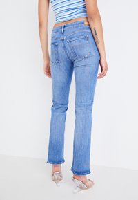 Jeans de color azul claro con un diseño de pierna recta, textura desgastada y bolsillos traseros. El dobladillo está ligeramente deshilachado. Llevados con zapatos de tacón transparente.