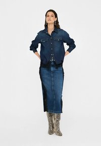 Jeans srajca z dvema prsnikoma, temno modre barve. Kombinirana z dolgo modro jeans krilo z čipkastimi stranskimi paneli in kovinskimi škornji z vzorcem kače.