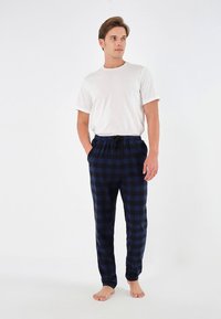 Pantalon de pyjama à carreaux bleu marine et noir avec une taille élastique et un cordon de serrage, associé à un t-shirt blanc à manches courtes uni.