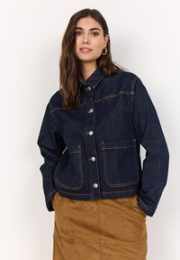 Mörkblå denimjacka med krage, knappfront och två stora framfickor. Har kontrasterande gula sömmar och en avslappnad passform.