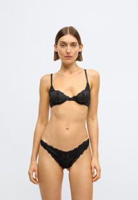 Czarny koronkowy biustonosz z kwiatowym wzorem i regulowanymi ramiączkami, zestawiony z pasującymi koronkowymi majtkami o falistym brzegu.