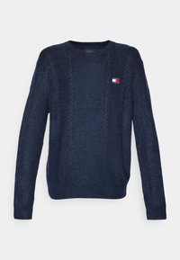 Pull en tricot bleu marine avec un motif de câble texturé. Il présente un col rond et un petit patch logo sur la poitrine. Manches longues.