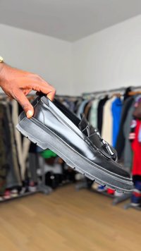Scarpa in pelle nera con suola in gomma chunky, finitura liscia e una fascia trasversale sulla parte superiore. Caratterizzata da punta arrotondata e suola testurizzata per una maggiore aderenza.