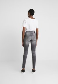 Jeans ajustados de tiro alto en gris con dos bolsillos traseros, combinados con una camiseta blanca de manga corta y unos zapatos negros tipo slip-on.