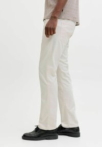 Pantaloni di cotone beige chiaro con vestibilità slim, tasche laterali e posteriori, abbinati a scarpe nere con lacci. Tessuto liscio e design minimalista.