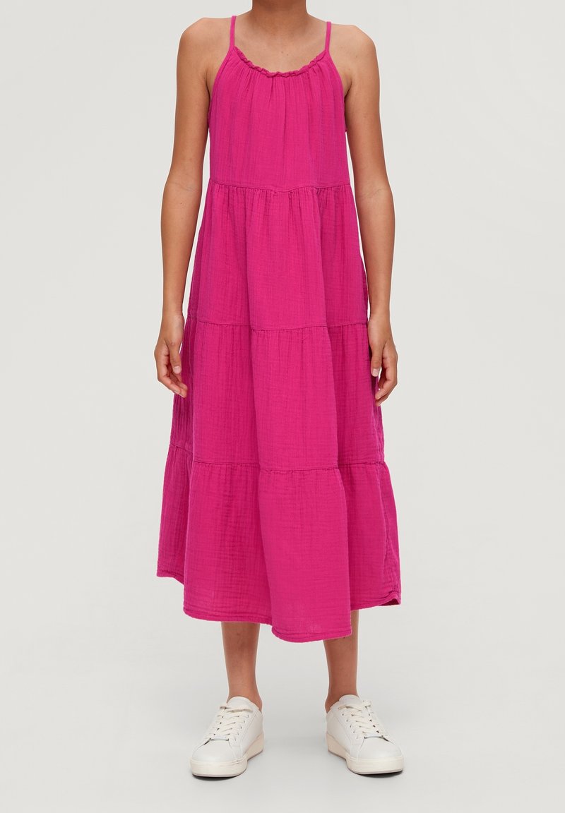 Vestido fucsia de capas con tirantes finos, hecho de una tela ligera. Se lleva con zapatillas blancas. Presenta un escote fruncido.