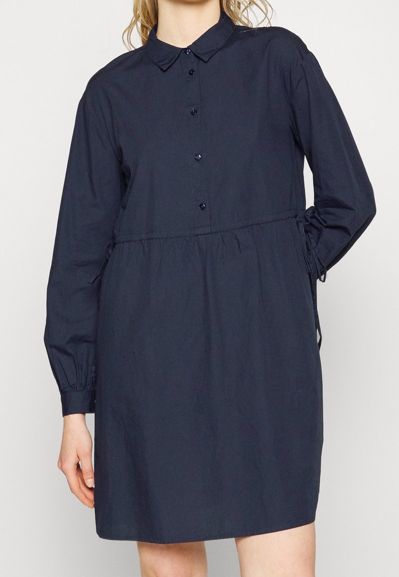 Mörkblå klänning med krage och knäppning framtill, långa ärmar, elastisk midja och samlade detaljer i sidorna. Smoothing, lätt tyg.