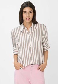 Chemise rayée marron et blanche avec un devant boutonné, des manches courtes et un col classique. Texture de tissu lisse. Un pantalon rose est visible.