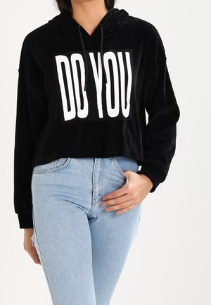 Felpa nera corta con testo bianco "DO YOU". Realizzata in morbido velluto, presenta cordini regolabili e maniche lunghe. Abbinata a jeans blu chiaro.
