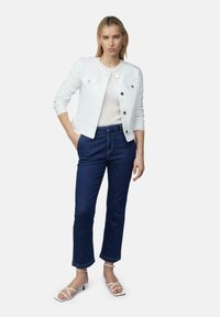Veste en denim blanc, top blanc côtelé, jeans droits bleu foncé, et sandales blanches à lanières. Lignes épurées et design classique avec un matériel minimal.