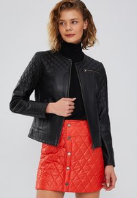 Zwarte leren jas met gequiltte schouders en ritszak, gecombineerd met een helderrode, gequiltte rok tot de knie met zilveren knopen.