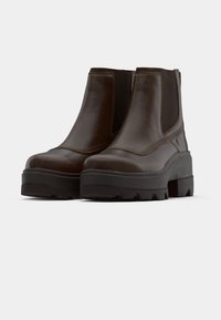 Bottines en cuir marron avec des panneaux élastiques sur les côtés, semelles épaisses en caoutchouc noir et détails de surface texturés. Conviennent pour un usage informel.