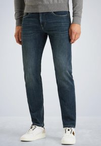 Donkerblauwe denim jeans met een slim fit, voorzien van subtiele vervaging, gestikte zakken en een stevige tailleband. Gecombineerd met witte sportschoenen.