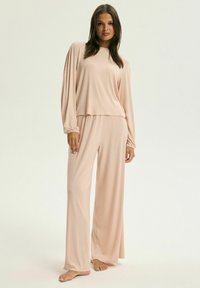 Jasnoróżowy zestaw wypoczynkowy składający się z bluzki z długim rękawem z marszczonymi mankietami oraz pasujących szerokich spodni w miękkim, gładkim materiale.