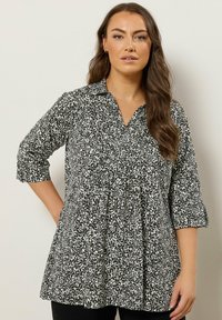 Tunic stampata in bianco e nero con scollatura a colletto, maniche a tre quarti e silhouette svasata. Tessuto leggero con un motivo testurizzato.