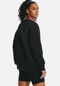 Sudadera negra de corte holgado, con puños y dobladillo acanalados, textura suave, cuello redondo y hombros caídos; combinada con shorts negros.