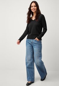 Maglione nero con scollo a V realizzato in tessuto morbido, abbinato a jeans in denim azzurro chiaro a gamba larga e ballerine nere, che mettono in evidenza un taglio rilassato.