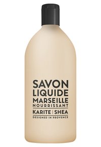 Płynne mydło w miękkiej beżowej butelce z czarną pompką. Wyraźny czarny napis brzmi "Savon Liquide Marseille Nourrissant Karite Shea."