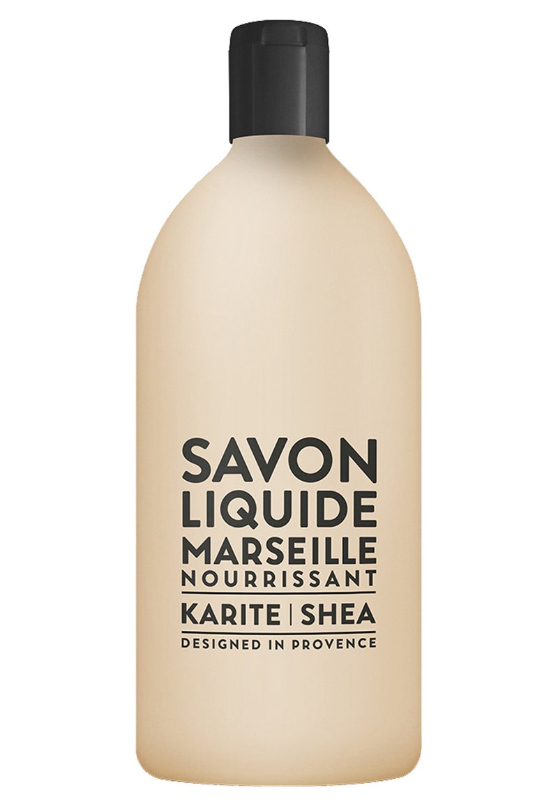 Flüssige Handseife in einer sanft beigen Flasche mit schwarzem Pumpverschluss. Auffälliger schwarzer Text lautet "Savon Liquide Marseille Nourrissant Karite Shea."